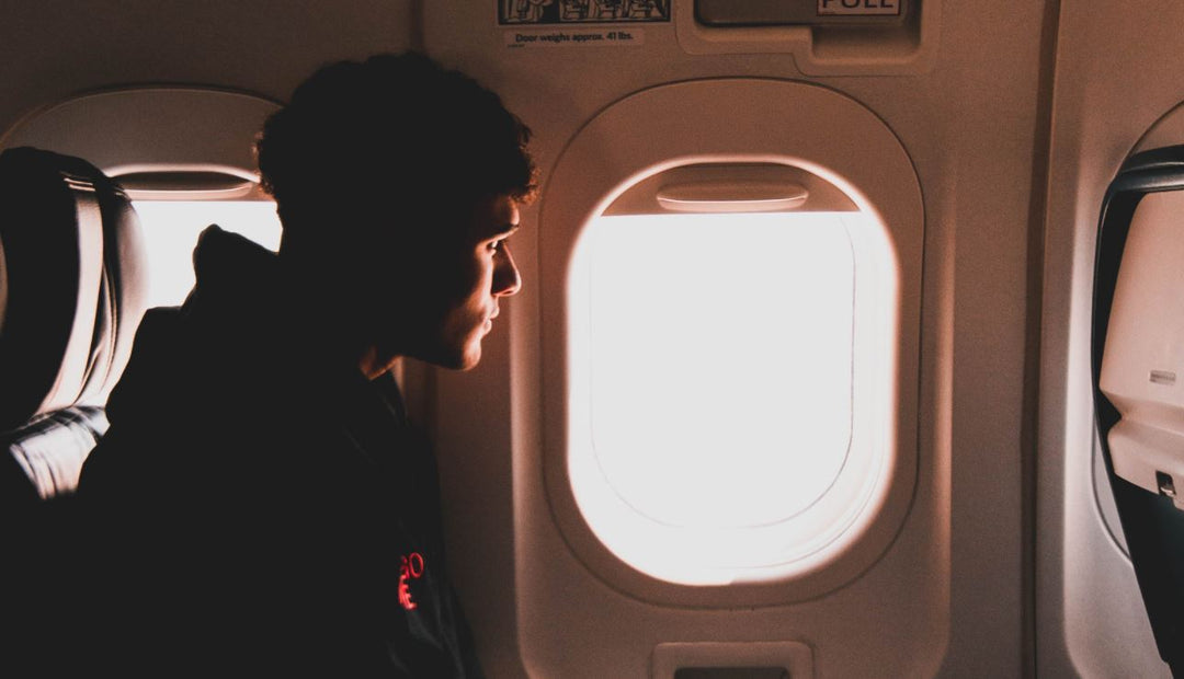 A young man with curly hair is seated on an airplane, looking out the window.