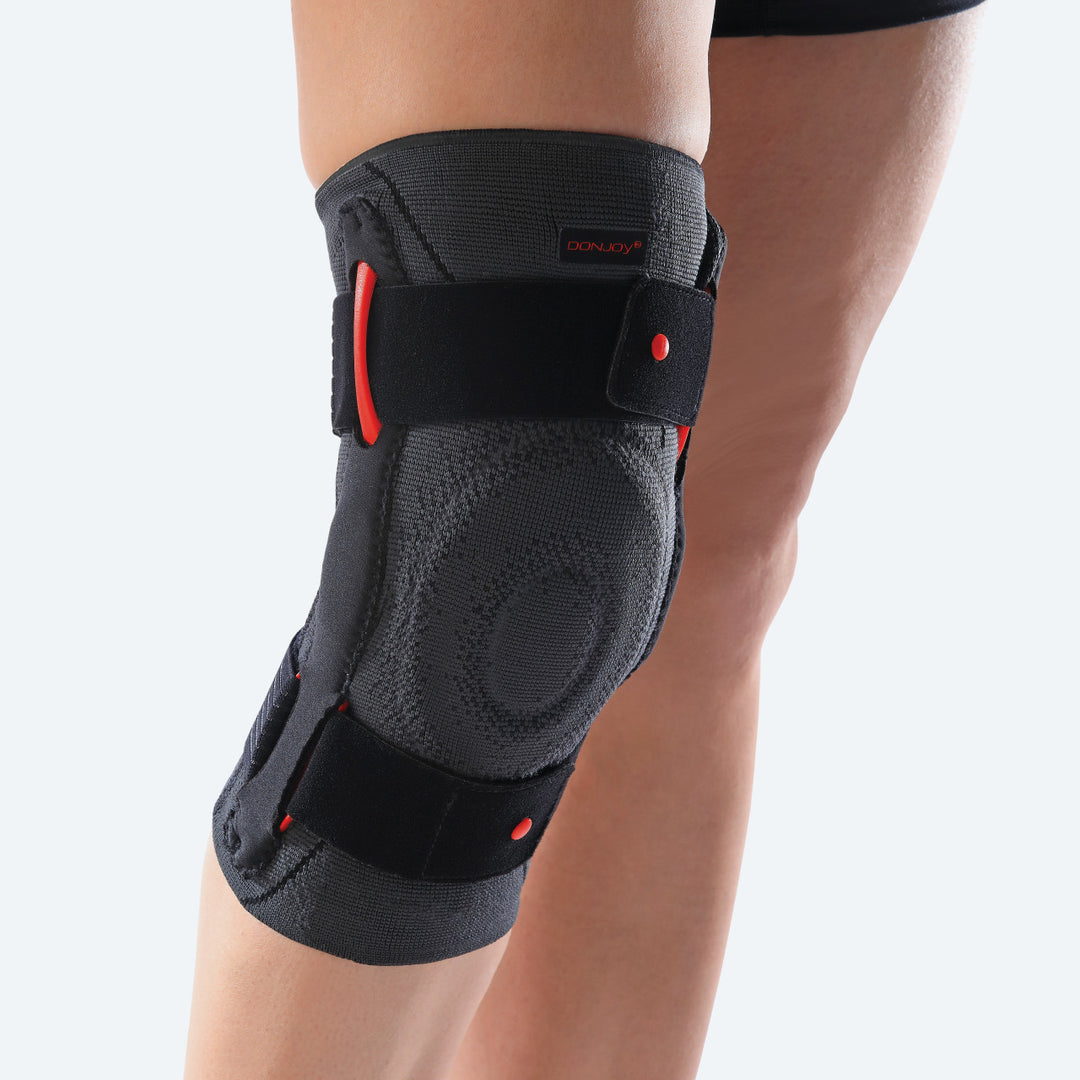 Black knee brace with red accents on a person's knee against a light gray background